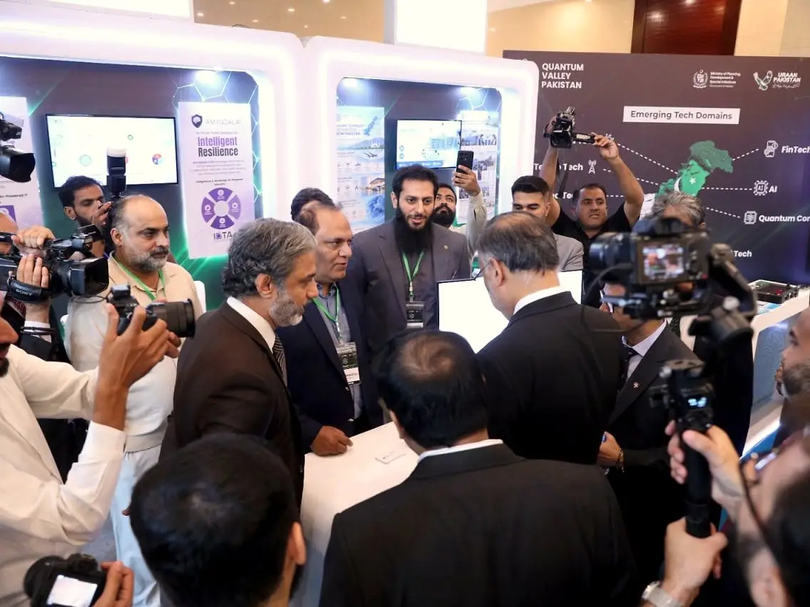 Usman with visitors and press cameras at a technology expo booth