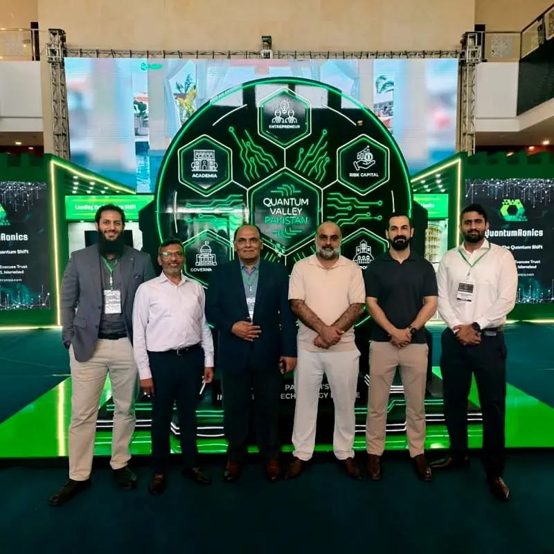 Usman with colleagues and guests in front of a lit stage at a technology expo