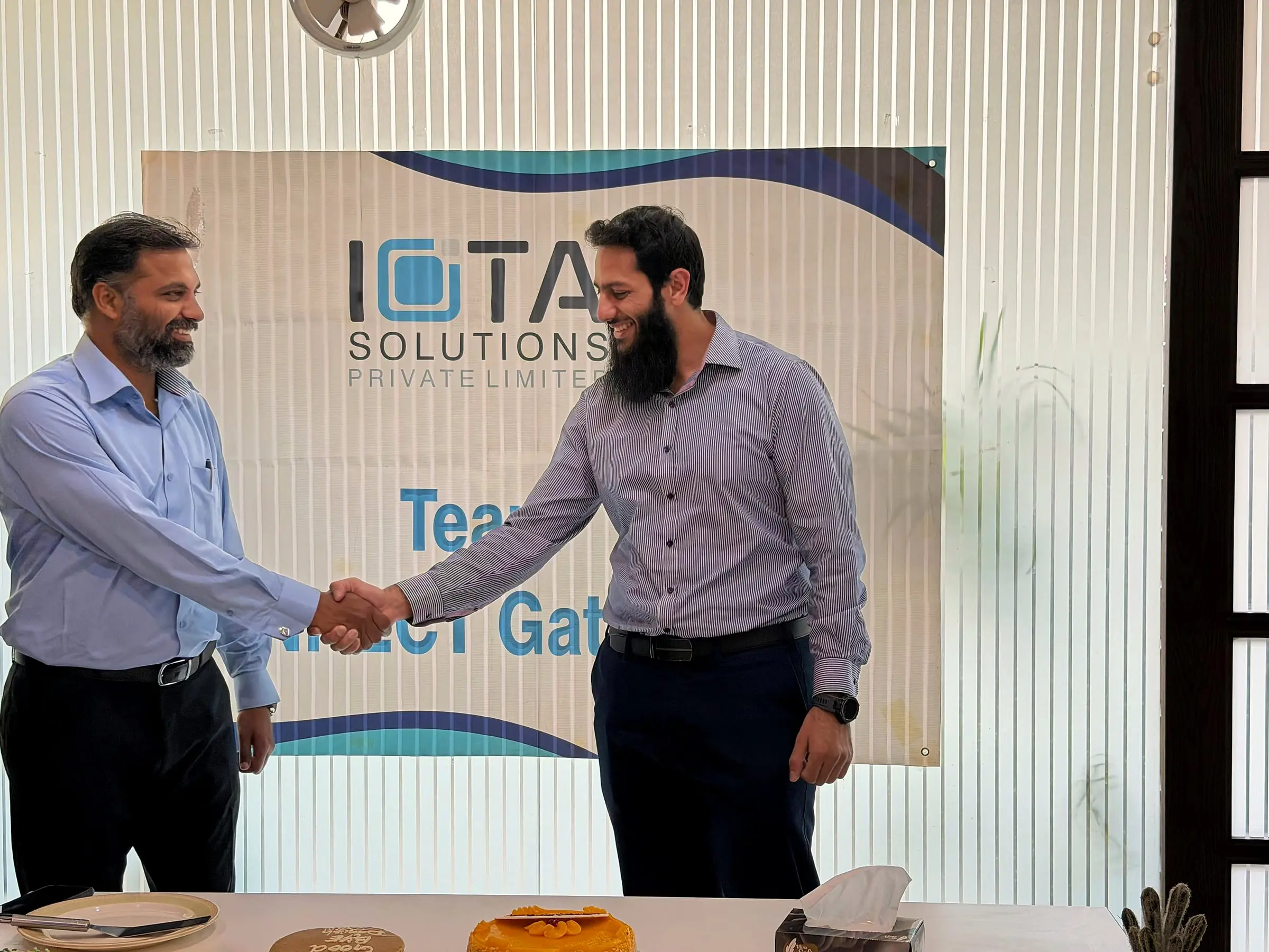 Usman shaking hands with a colleague in front of an IOTA Solutions banner