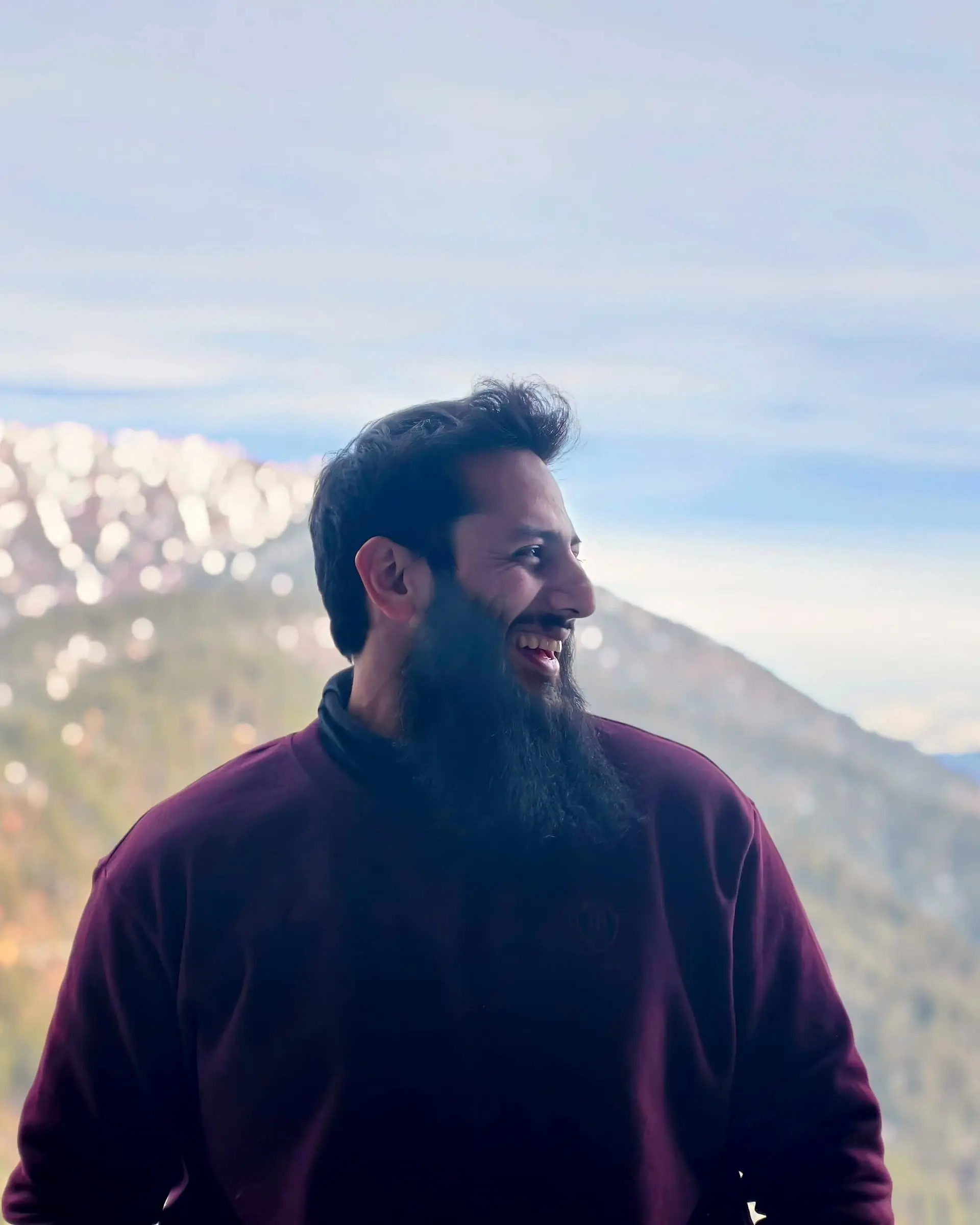 Usman smiling in the hills, snow on the peaks behind him