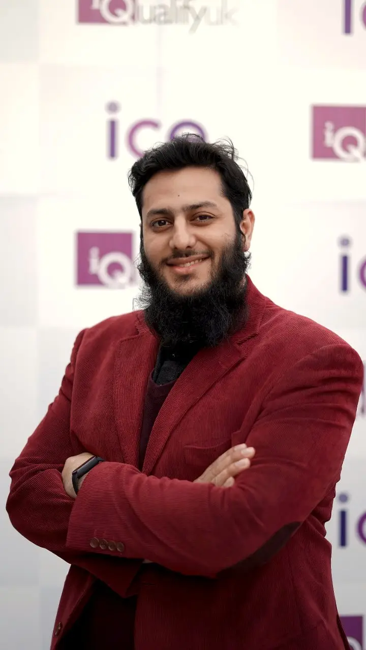 Usman in a red blazer, arms crossed, in a training room